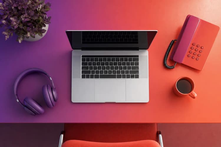 Mesa com um laptop, telefone e fones de ouvido.