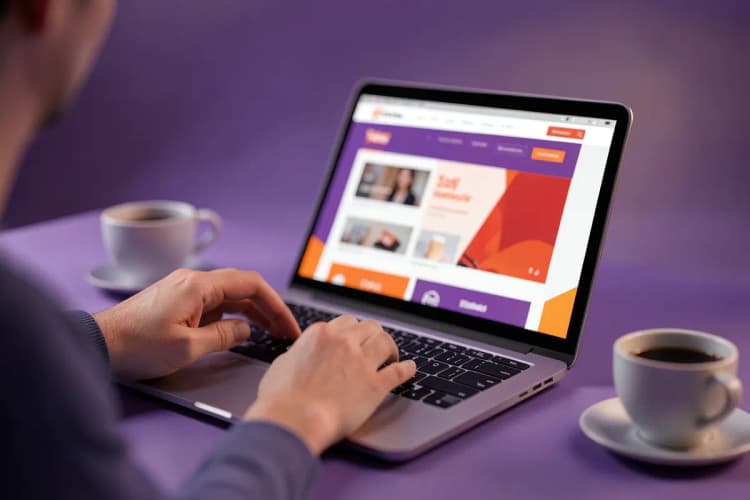 Uma pessoa usando um notebook para navegar em um site de vendas, com uma xícara de café ao lado.
