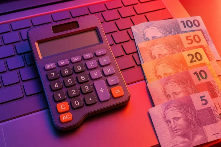 Calculadora sobre um teclado de computador com notas de dinheiro ao lado.
